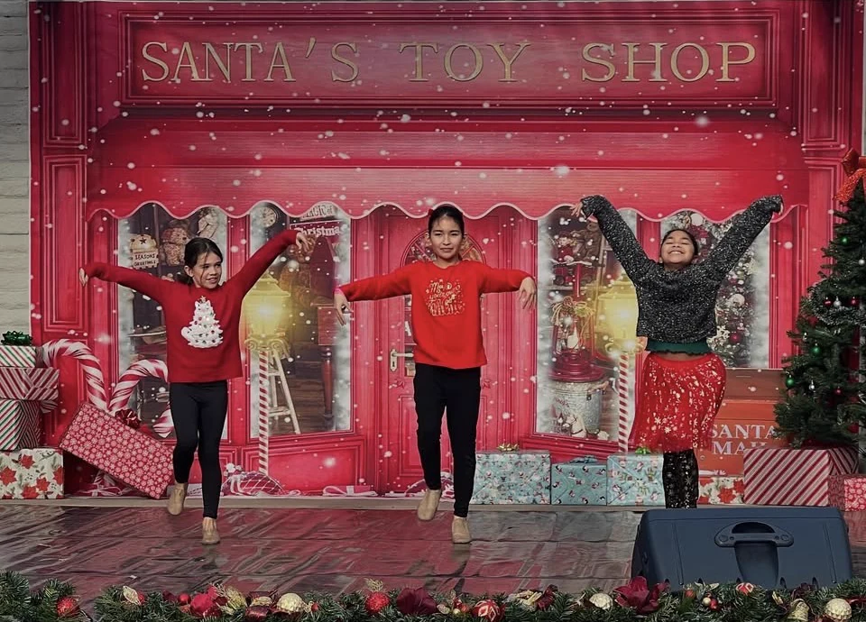 Three Serendipity dancers performing in front of a festive Santa's Toy Shop backdrop at the Winter Showcase