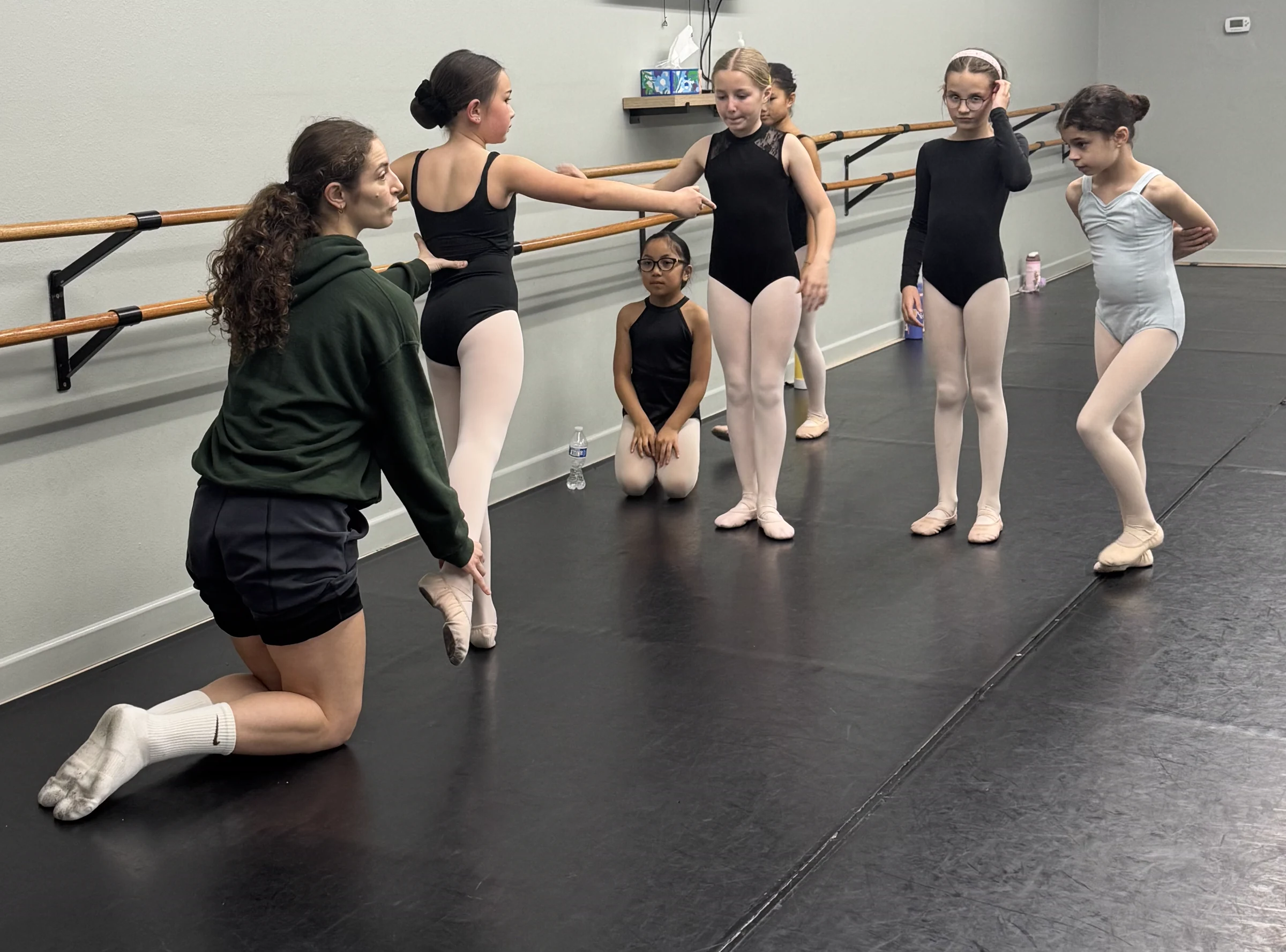A Serendipity teacher kneeling beside a ballet student to help with her position while classmates watch